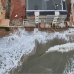 La indignació veïnal i la preocupació pel futur de la costa han tornat a prendre el passeig marítim de Tavernes de la Valldigna en una nova jornada de protestes. Centenars de residents s'han mobilitzat per a exigir a la Direcció General de Costes la regeneració urgent del seu litoral, greument afectat per la pèrdua d'arena i l'amenaça directa del mar sobre els habitatges. TAVERNES DE LA VALLDIGNA. 23 d'agost de 2026.— El malestar veïnal i la preocupació mediambiental han tornat a prendre els carrers de Tavernes de la Valldigna. Centenars de residents s'han mobilitzat aquest cap de setmana per a alçar la veu davant el que consideren una situació insostenible: la paulatina i imparable desaparició del seu front litoral a causa dels successius temporals marítims que afecten la zona. La pèrdua de superfície de platja ha aconseguit nivells sense precedents en el municipi. Segons els últims informes tècnics i mesuraments locals, algunes seccions de la costa han perdut fins a un 77% de la seua massa d'arena original, deixant el ferm de les zones habitades exposat a l'embat directe de l'onatge. Habitatges en perill i desallotjaments preventius La gravetat de l'erosió ha deixat de ser una mera pèrdua d'atractiu turístic per a convertir-se en un problema de seguretat pública. Els últims episodis de marejada i fort onatge van provocar l'esfondrament de murets de protecció i la infiltració d'aigua en les infraestructures costaneres, una situació que va obligar les autoritats locals a evacuar d'emergència diversos habitatges situats en primera línia de mar. Els propietaris afectats denuncien que la falta d'arena ha après el matalàs natural que abans amortia la força de les ones, deixant les fonamentacions directament exposades a la violència de la mar. Exigències a les administracions i silenci municipal La marxa pacífica va recórrer el passeig marítim exigint solucions definitives a la Direcció General de Costes i al Ministeri per a la Transició Ecològica. Els col·lectius veïnals reclamen superar la fase dels "parches d'emergència" —basats en l'aportació puntual d'arena que els temporals tornen a arrossegar— i executar projectes d'enginyeria de regeneració litoral duradors, com ara la instal·lació d'espigons o barreres submarines. Per la seua banda, el govern local ha evitat fer cap mena de publicitat de la convocatòria. Aquesta actitud manté la línia de l'alcaldessa, de signe socialista, qui igual que va evitar enfrontar-se amb el ministre Óscar Puente per a exigir la represa de les obres de l'estació d'ADIF, evita ara enfrontar-se amb els seus companys de partit a la Direcció General de Costes i a la Delegació del Govern. Els veïns, mentrestant, temen que l'arribada dels temporals de tardor i hivern cause danys estructurals irreparables a la localitat.